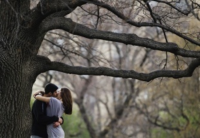 A couple kisses while standing underneath a tree inside Central Park during a warm day in New York