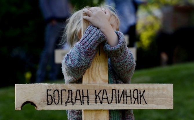 Un copil îmbrățișează o cruce la comemorarea victimelor războiului din Ucraina. Foto: Enca.com